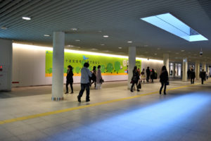 北海道の札幌駅前地下歩行空間（チカホ）の道路で、大きなデザイン画が貼られたサイドスペースを行き交う人々の様子